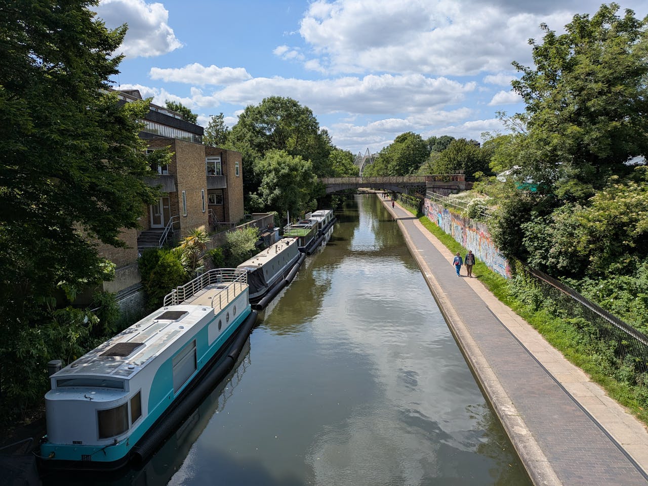 A peaceful canal scene in Camden, London, featuring houseboats and a scenic walkway under a blue sky.