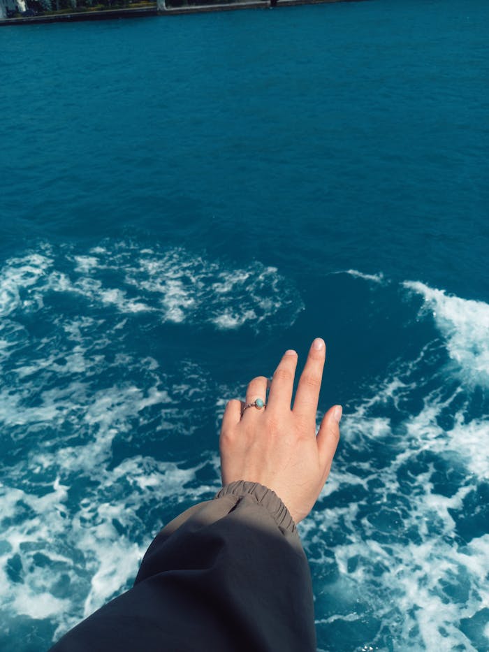 A hand extended over moving ocean waves, creating a sense of freedom and connection with nature.