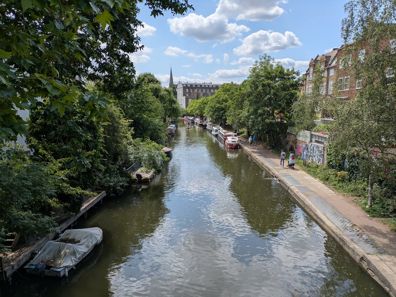 Scenic canal in London with boats and greenery, captured on a sunny day. Perfect for travel and nature enthusiasts.